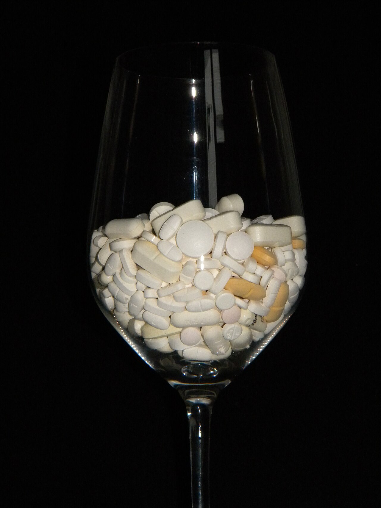 Assorted medicine tablets and capsules in a glass